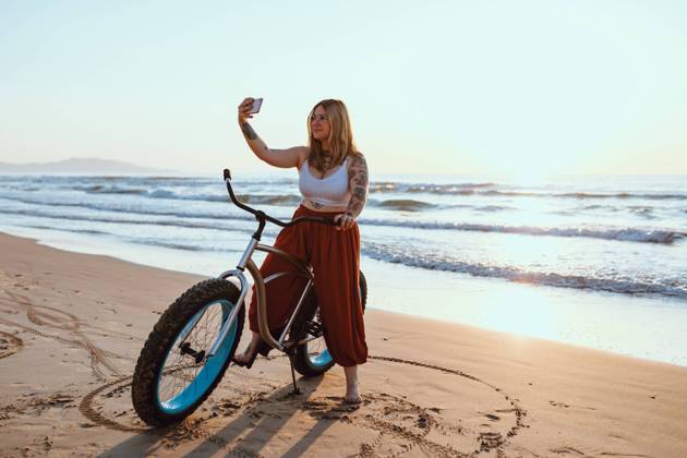 Cheerful chubby woman taking selfie on smartphone while resting with bicycle at sunny shore, Model released, Property released Copyright: xAdrianxSavax MR