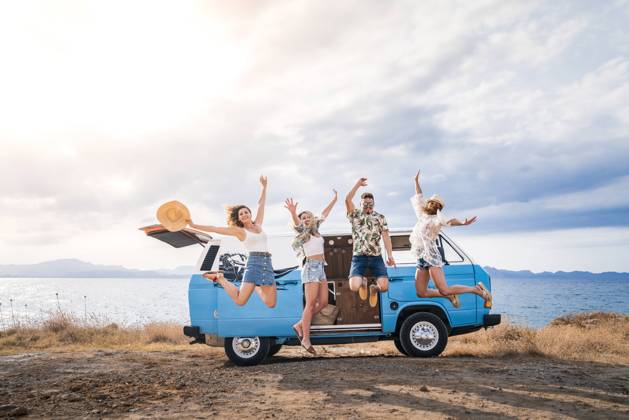 Cheerful tourist jumping raising hands and legs on background of bright minivan on beach in sunny day Copyright: xJuanxMiguelxApariciox Model Released