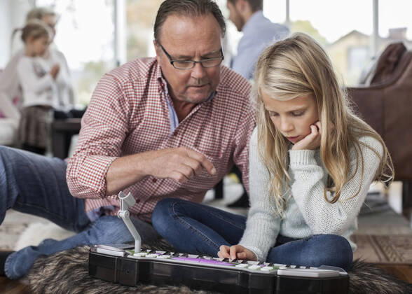 IMAGO Creative: Bildung, Musikerziehung Grandfather and granddaughter playing piano with family in background at home , model released Copyright: xMaskotx , MA38866