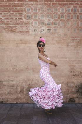 Side view of eccentric cheerful woman in colorful pink costume smiling and dancing by brick wall on sunny day Copyright: xEduardoxLopezx Model Released