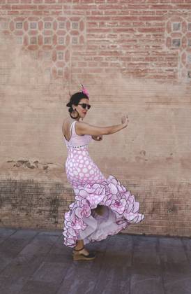 Side view of eccentric cheerful woman in colorful pink costume smiling and dancing by brick wall on sunny day Copyright: xEduardoxLopezx Model Released