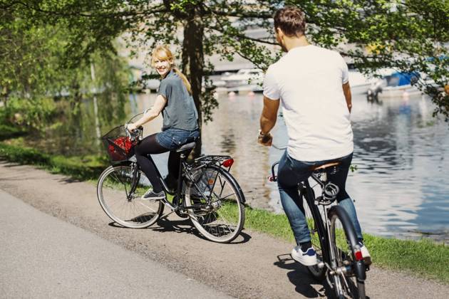 IMAGO Creative, Jahreszeit Sommer, Sommer in der Stadt Happy businesswoman looking at colleague while riding bicycles on street by lake , model released Copyright: xMaskotx , MA45531