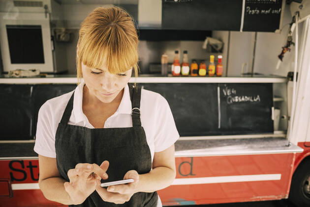 Close-up of female chef using mobile phone against food truck , model released Copyright: xMaskotx , MA48213