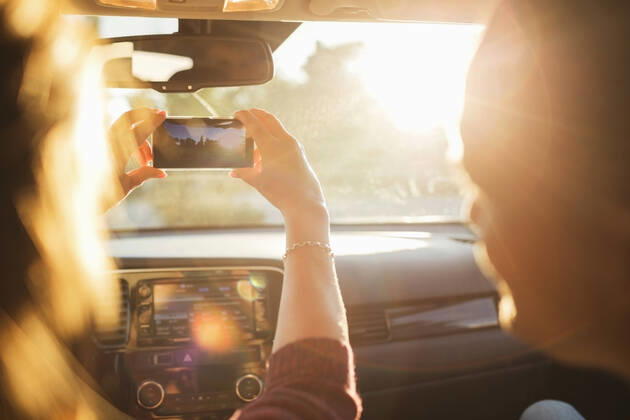 IMAGO Creative: Klimawandel - Nachhaltiges Reisen Man looking at woman photographing from mobile phone through car windshield , model released Copyright: xMaskotx , MA53205