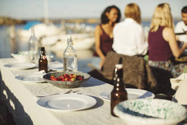 Fruits with plates and bottles on table against friends at harbor during sunny day , model released Copyright: xMaskotx , MA58590