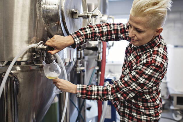 Confident female manager pouring beer from storage tank at factory , model released, property released Copyright: xMaskotx , MA62529