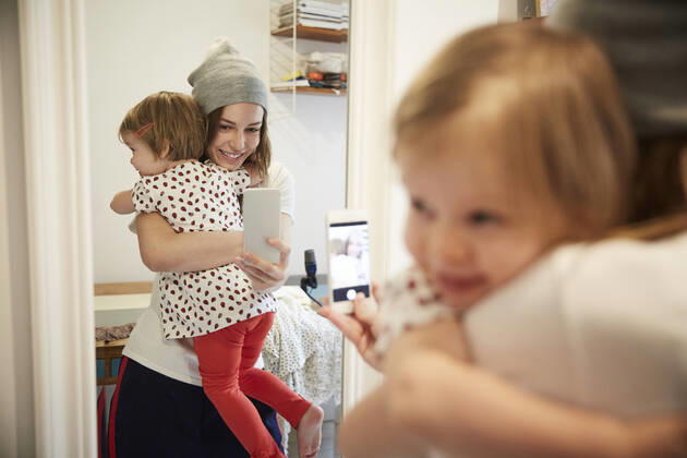 Smiling podcaster taking selfie with daughter through smart phone while reflecting on mirror , model released, property released Copyright: xMaskotx , MA64772