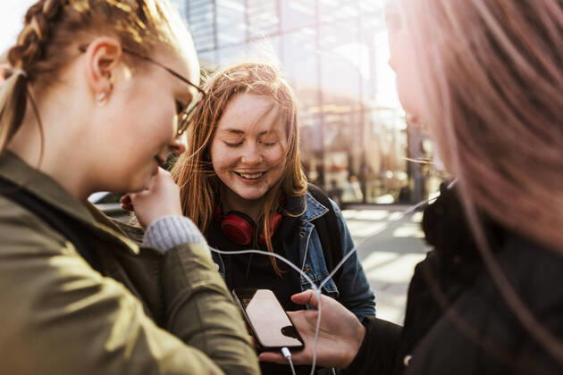 Teenage girl looking at friends listening music through mobile phone in city , model released Copyright: xKentarooxTrymanx , MA64898