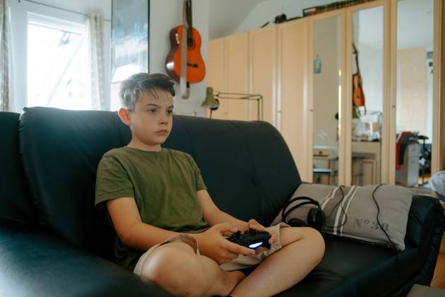 Concentrated little boy in casual clothes sitting on sofa with crossed legs and playing video game with joystick Copyright: xJakexJakabx Model Released