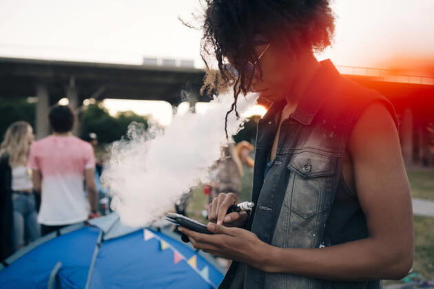 Side view of young man smoking while using mobile phone at music event , model released Copyright: xMaskotx , MA69798