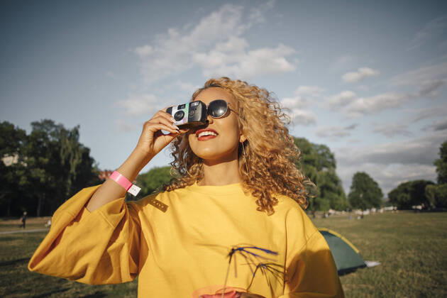 Smiling young woman photographing with camera on field against sky , model released Copyright: xMaskotx , MA69868