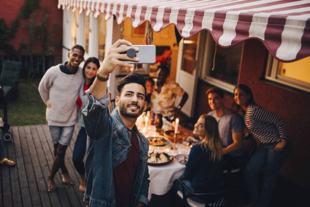 Smiling young man taking selfie with friends during dinner party , model released, property released Copyright: xMaskotx , MA70328
