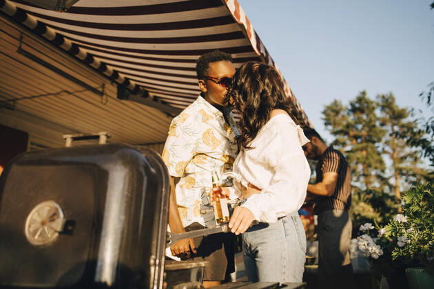 Girlfriend kissing boyfriend while standing by barbecue grill in party , model released, property released Copyright: xMaskotx , MA70409