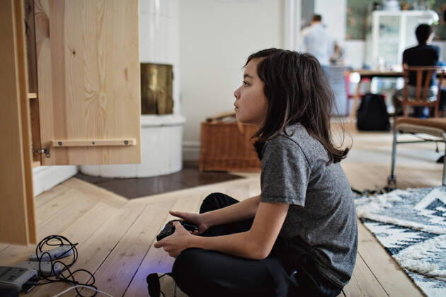 Side view of boy looking away while playing video game on hardwood floor at home , model released, property released Copyright: xMaskotx , MA71163