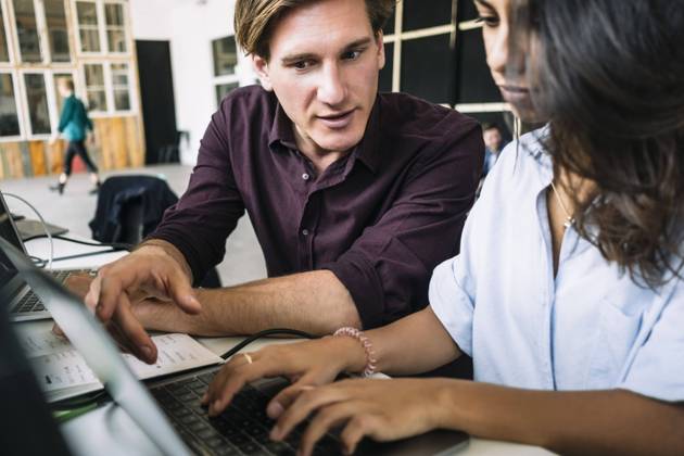 Confident male IT professional discussing with female hacker using laptop at desk in creative office , model released, property released Copyright: xMaskotx , MA71687