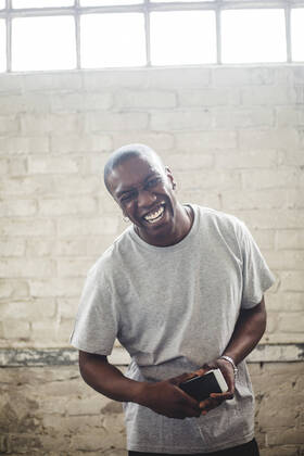 Portrait of cheerful male IT expert holding mobile phone while standing against brick wall in office , model released, property released Copyright: xMaskotx , MA71719