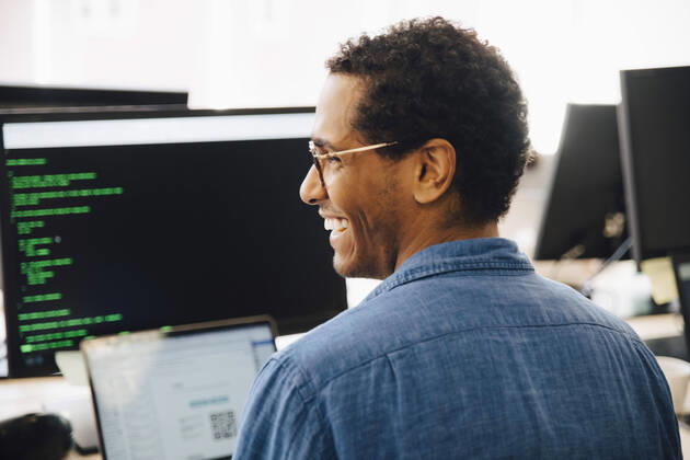 Rear view of cheerful male it professional looking away while sitting in creative office , model released, property released Copyright: xMaskotx , MA72458
