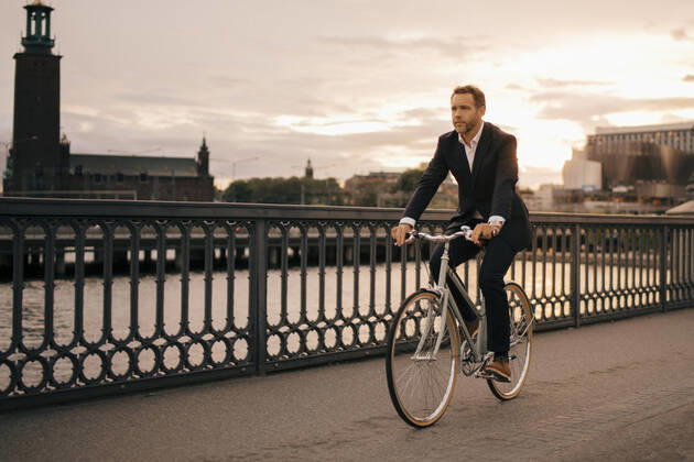 Full length of businessman cycling on bridge in city during sunset , model released Copyright: xMaskotx , MA74408