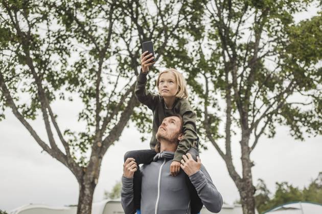 IMAGO Creative, Jahreszeit Sommer, Sommerferien Girl holding mobile phone while sitting on father s shoulders against trees , model released, property released Copyright: xMaskotx , MA74510