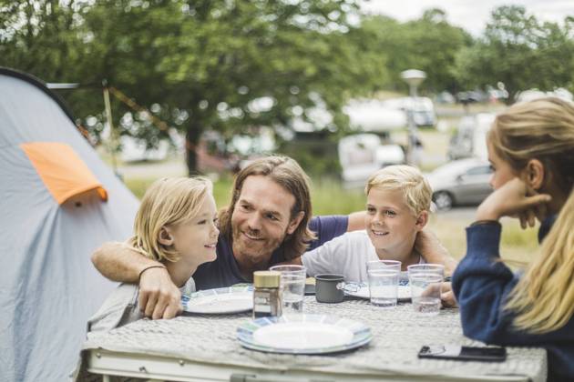 IMAGO Creative, Jahreszeit Sommer, Sommerferien Smiling father sitting with children at table in camping site , model released, property released Copyright: xMaskotx , MA74548