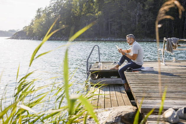 Full length of man using digital tablet while sitting on wooden pier over lake at forest , model released, property released Copyright: xMaskotx , MA74640