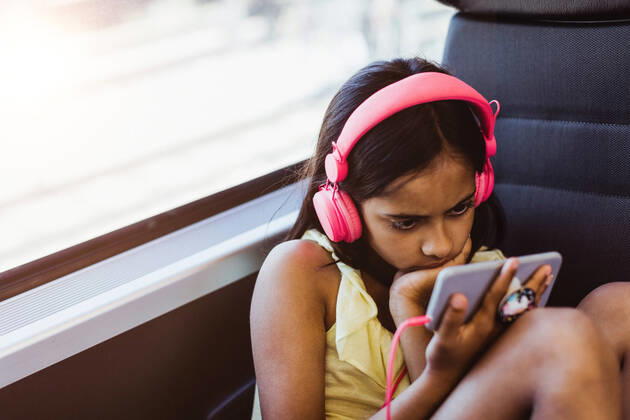 Girl wearing pink headphones watching movie on mobile phone while sitting by window in train , model released, property released Copyright: xMaskotx , MA74687
