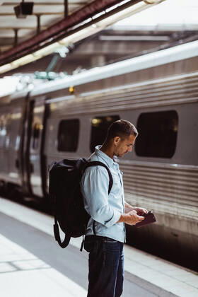 IMAGO Creative: Business, Innovative Technologie-Lösungen Mid adult man with backpack using mobile phone while standing by train on platform , model released, property released Copyright: xMaskotx , MA74702