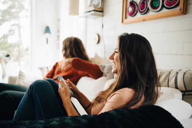 Smiling woman with smart phone looking away while sitting with friend on sofa at home , model released, property released Copyright: xMaskotx , MA75221