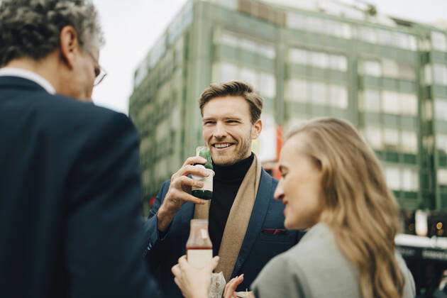 IMAGO Creative: Corporate: Klimaschutz, Digitalisierung und Urbanisierung Smiling male entrepreneur with drink looking at coworkers in city Germany, Hamburg, model released Copyright: xMaskotx , MA79088