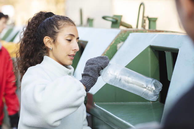 IMAGO Creative: Klimawandel - Umwelterziehung Smiling female environmentalist with friend throwing plastic bottle in garbage can Sweden, Stockholm, model released Copyright: xMaskotx , MA81932