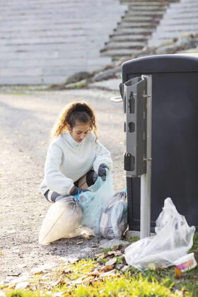 IMAGO Creative: Klimawandel - Umwelterziehung Female volunteer crouching with plastic waste by garbage can Sweden, Stockholm, model released Copyright: xMaskotx , MA81949