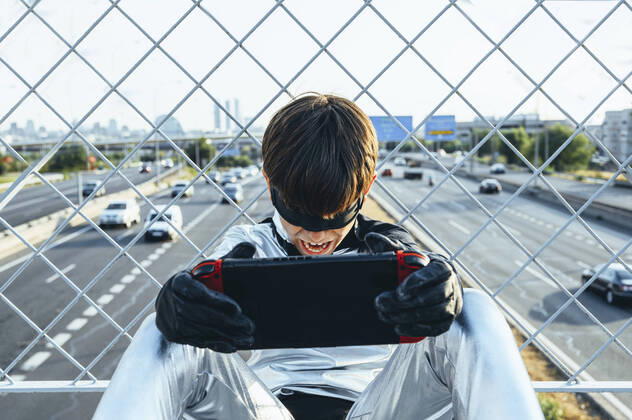 Screaming boy disguised as superhero using games cosole above the streets of the city model released Symbolfoto JCMF00213
