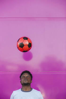 Young man juggling with soccer ball against pink wall in city model released Symbolfoto LJF01679