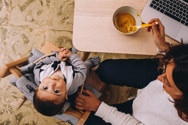 From above modern young female remote worker feeding little child while sitting at table with laptop and working on online project Copyright: xMaciaxPuiggrosx Model Released
