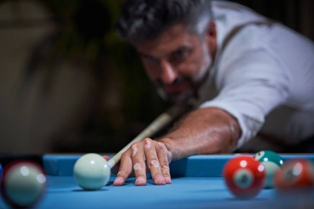 Confident focused gray haired male in white shirt preparing for shot with cue while playing billiards game Copyright: xPhilippexDegrootex Model Released