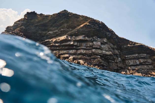 IMAGO Creative, Jahreszeit Sommer, Sommerferien Sea wave glistens in sunlight in front of high rocky cliff on sunny summer day Copyright: xPhilippexDegrootex Model Released