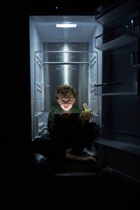 Calm relaxed kid sitting in empty fridge with ripe banana and using digital tablet at hot night Copyright: xPhilippexDegrootex Model Released