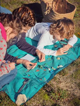 IMAGO Creative: N?chste Generation, Sozial- und klimabewusst Young lady with pencil writing in notebook and children gauging by ruler little plastic things and lying on coverlet on ground Copyright: xPhilippexDegrootex Model Released