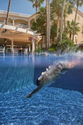 IMAGO Creative, Jahreszeit Sommer, Sommerferien Underwater side view of anonymous tourist diving down into swimming pool with blue clear water during summer holidays in tropical resort, Model released, Property released Copyright: xPhilippexDegrootex MR