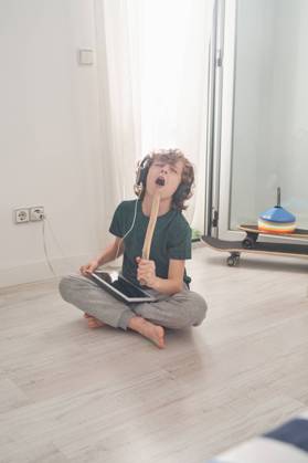 Cheerful preteen boy in headphones and casual clothes singing with closed eyes while using digital tablet in light modern room Copyright: xPhilippexDegrootex Model Released
