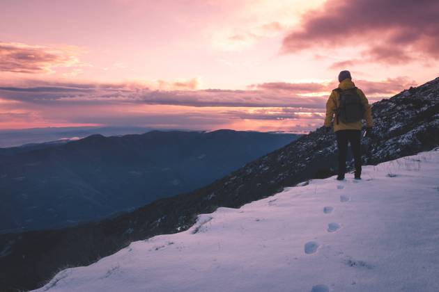 Back view of unrecognizable man in warm clothes standing on white snow and looking at cloudy sunset sky while traveling through mountains in countryside Copyright: xPolxSolex Model Released
