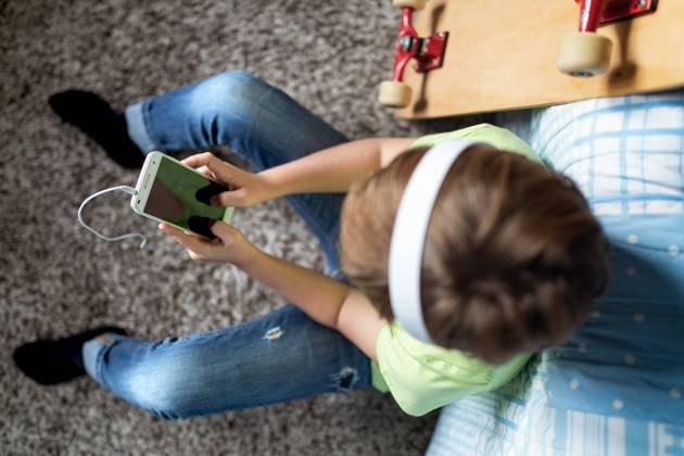 little boy with headphones listening to music and chatting with friends in social network while sitting near skateboard in bedroom Copyright: xSergioxVictorxVegax Model Released