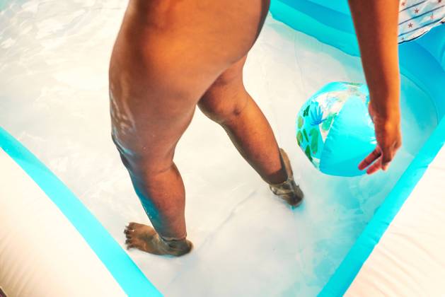 From above of crop black female standing in pool with inflatable ball while chilling during party Copyright: xVictorxBorderax Model Released