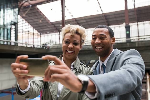 Elegant trendy black coworkers laughing happily while taking selfie with smartphone on station., Model released Copyright: xWidetapex MR