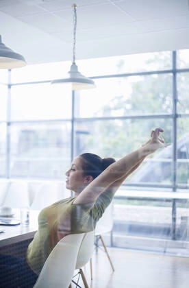 Tired young businesswoman stretching arms while sitting at desk in office model released Symbolfoto property released AJOF00737