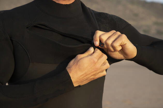 Man zipping black wetsuit at beach model released Symbolfoto KBF00630