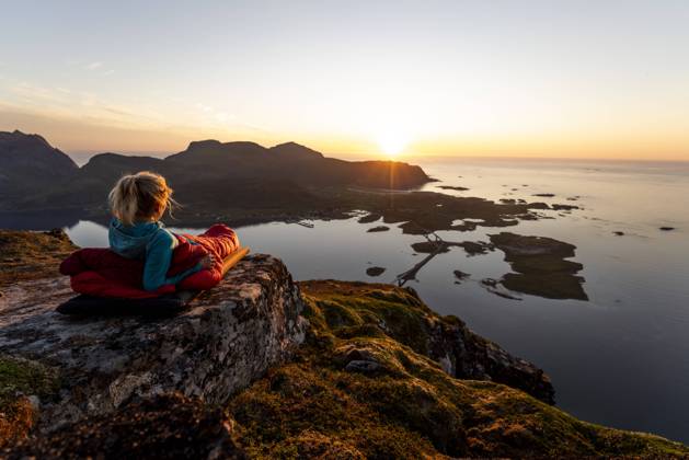 Hiker admiring sunset view while lying in sleeping bag at Volandstinden, Lofoten model released Symbolfoto MALF00248