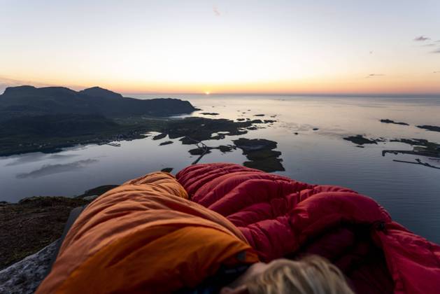 Hiker lying in sleeping bag against sea at Volandstinden, Lofoten, Norway model released Symbolfoto MALF00252