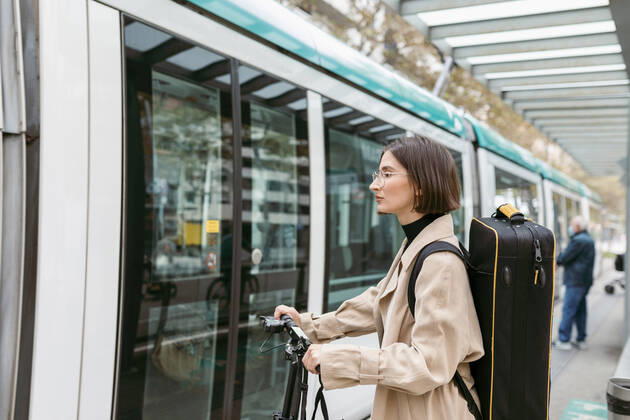 Woman with instrument case and electric push scooter standing by tram in city model released Symbolfoto VABF03969