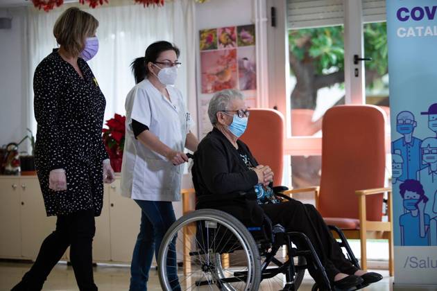 Josefa PÃ rez, 89 years old, accompanied by a health worker, is the first woman to be vaccinated in Catalonia, during the first day of vaccination in Spain, in the Feixa Llarga retirement home in L Hospitalet de Llobregat, in Barcelona (Spain), on 27 December 2020. The first doses of the vaccine developed by Pfizer and BioNtech laboratories arrived in Spain yesterday, December 26, at a Pfizer warehouse in Guadalajara by land from Puurs (Belgium). Starting Monday, weekly deliveries will be made to the autonomous communities with an average of 350,000 doses prioritized for four population groups: residents and health and social-health personnel in homes for the elderly and disabled; front-line health personnel; other health and social-health Copyright: xPauxVenteox 3494895